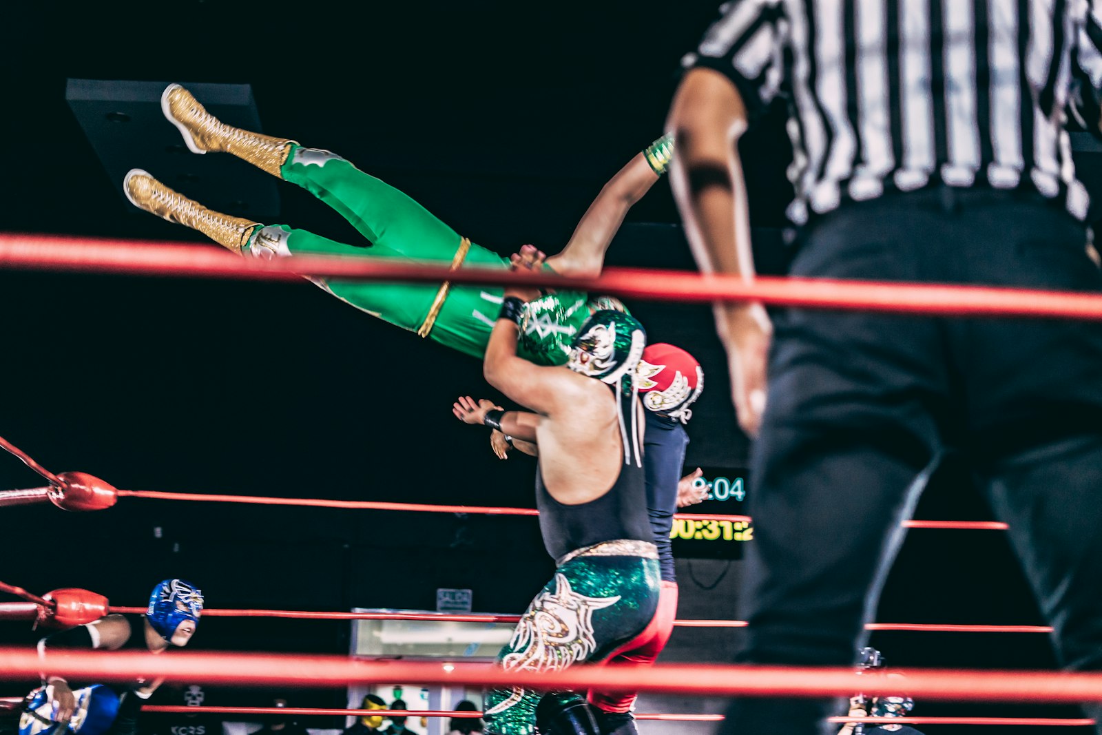 Incontro di wrestling sul ring sotto le luci, con l'arbitro e il pubblico